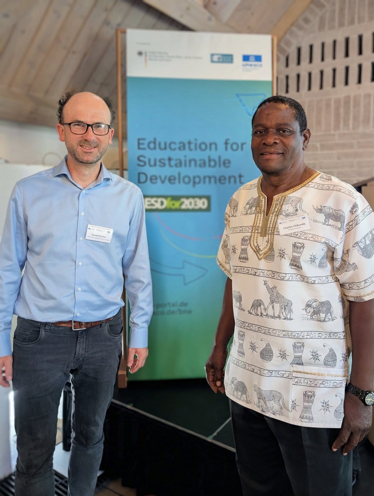 Daniel Fischer and Dr Charles Chikunda in front of the ESD for 2030 banner at the Munich symposium